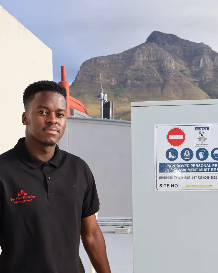 A SecaTeq FM technician on a rooftop, with the mountain behind him.