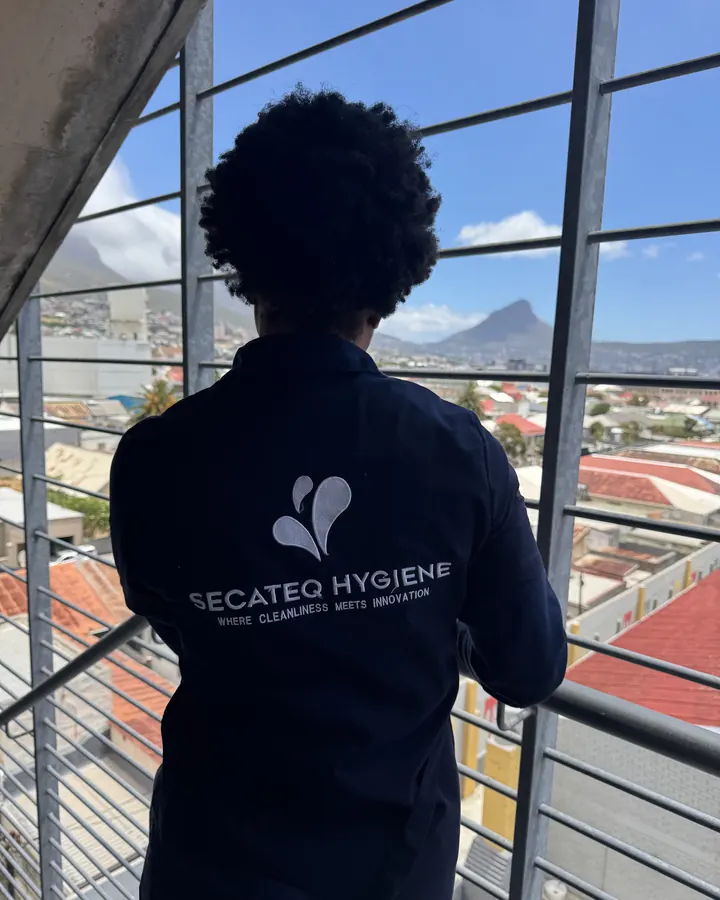 A SecaTeq Hygiene team member seen from behind, the SecaTeq Hygiene logo on her jacket, looking out over the city.