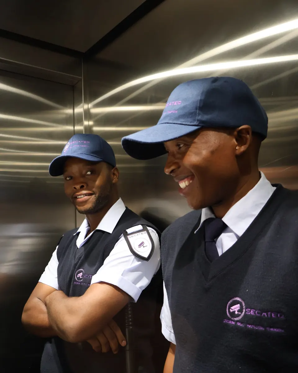 Two smiling SecaTeq security officers in uniform, standing in a lift.