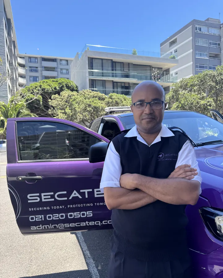 A SecaTeq security officer with his arms folded, beside a purple SecaTeq vehicle.